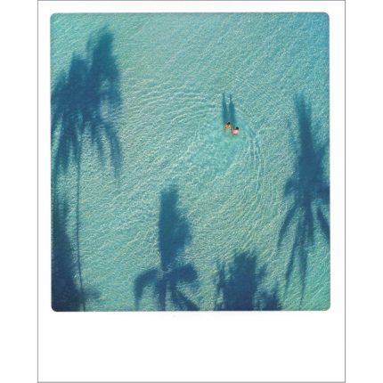 ALT-Text Postkarte von Aquarupella aus der Serie Bon Voyage. Auf der Fotografie sieht man von oben zwei Menschen im Wasser laufen von Palmenschatten umringt