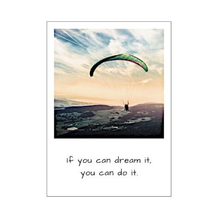 Eine Postkarte in Stil eins Polaroid Bildes. Das Foto zeigt eine Paraglider in der Luft bei Sonnenuntergang. Spruch: if you can dream it, you can do it.